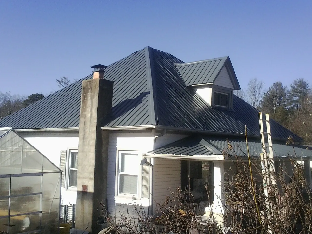 Dark blue standing seam metal roof on a white farmhouse with dormer — Slate & Tile Roof Repair by Roofing Brothers in Partlow