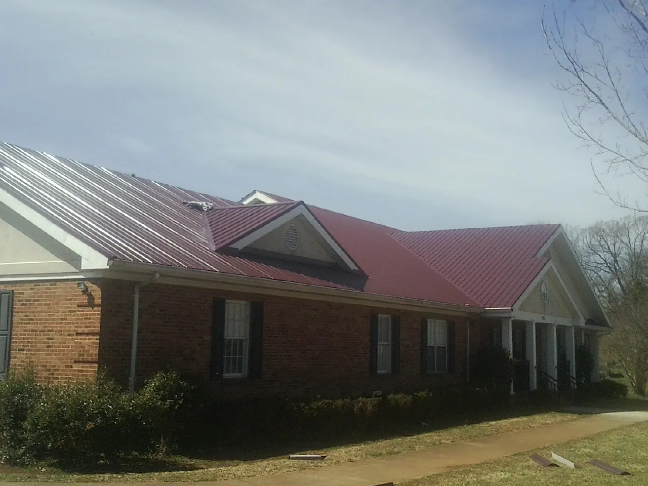 Red metal roof with gabled entries on a long brick building, from a Hail Damage Roof Repair job in Partlow