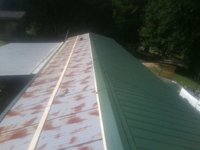 Old rusted panels beside newly installed green metal roofing — Wind Damage Roof Repair by Roofing Brothers in Partlow