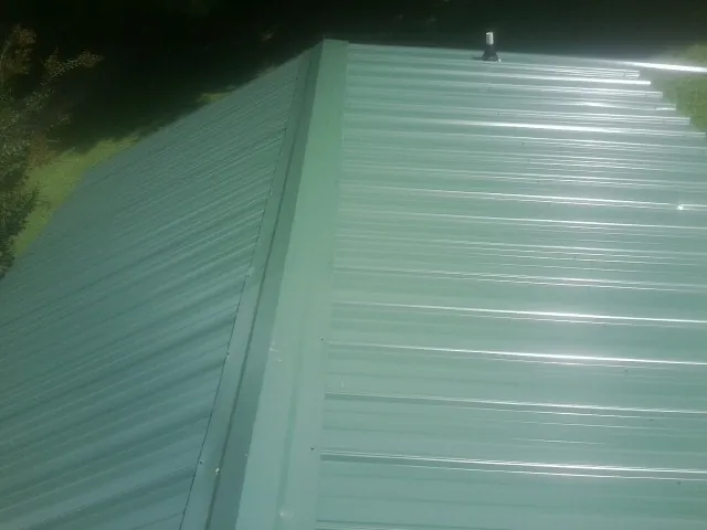 New green metal panels meeting at the ridge of a roof — Flat Roof Repair work by our crew in Partlow