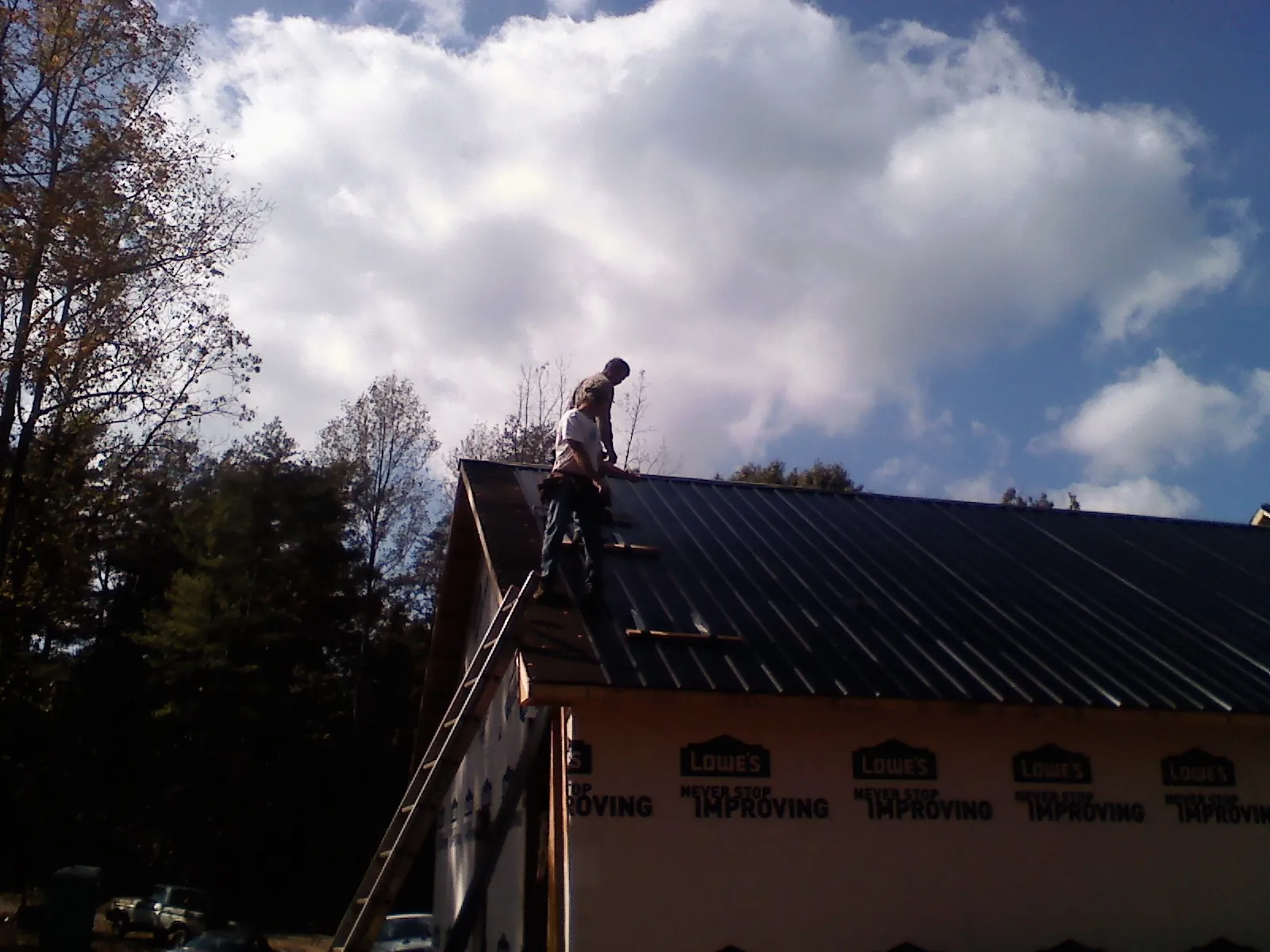 Roofer fastening dark metal panels high against a cloudy sky, from a Roof Inspection job in Partlow